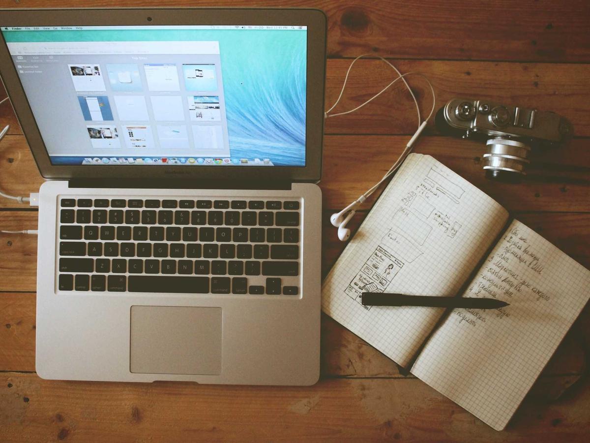 A laptop and an open notebook with handwritten notes on a wooden desk