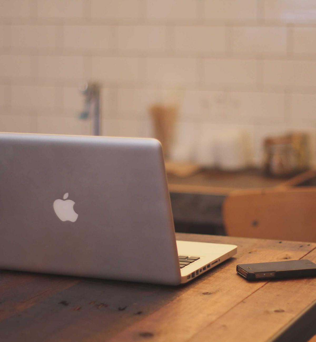 A laptop open on a wooden table in a bright room