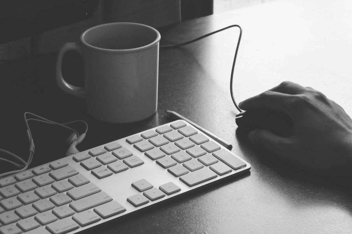 A hand on a computer mouse beside a keyboard and a coffee mug
